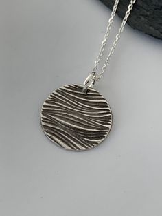 This minimalist tiny ocean necklace has been entirely handmade using .999 fine silver. It has been cut out from fine silver precious metal clay, textured, fired and oxidized. The pendant hangs from a sterling silver diamond cut cable chain. This fine silver pendant features an embossed waves textured pattern on one side of the pendant and is reversible to a completely different waves embossed pattern on the reverse side. Pendant size: approximately 1/2 x 1/2 inches Chain length: adjustable at 16 Minimalist Etched Round Pendant Necklace, Minimalist Etched Necklaces For Everyday Wear, Minimalist Etched Necklaces, Minimalist Everyday Etched Necklaces, Minimalist Everyday Etched Necklace, Minimalist Etched Round Pendant Jewelry, Adjustable Sterling Silver Etched Necklace, Minimalist Round Etched Necklace, Minimalist Stamped Pendant Jewelry