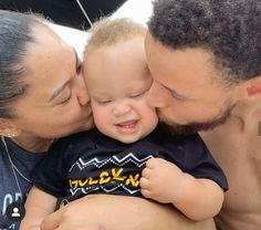 a man and woman kissing a baby on the cheek with an umbrella in the background