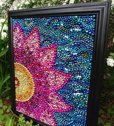 a painting made out of beads with a sun and flower on it's side