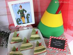 a table topped with desserts covered in green and yellow frosting next to a sign that says elf