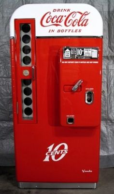 an old fashioned coca - cola machine sitting in front of a wall