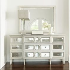 a white dresser sitting next to a mirror on top of a wooden floor