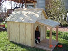 a dog house made out of wood with a roof on the grass in front of a house