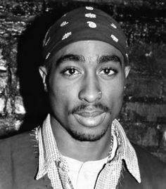 a black and white photo of a man wearing a hat in front of a brick wall