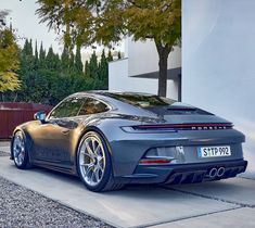 a grey porsche sports car parked in front of a white building with trees behind it