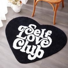 a black heart shaped rug with the words love club on it in white letters, next to a chair