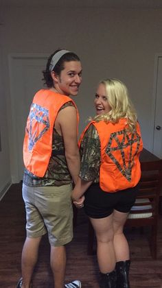 two people wearing orange vests and black shorts standing next to each other in a room