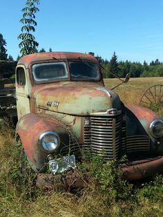 an old rusted truck sitting in the middle of a field