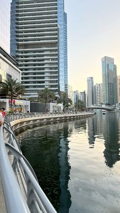 people are walking along the water in front of tall buildings