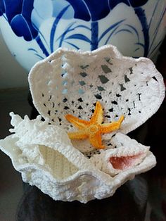 two crocheted shells are sitting on a table next to a blue and white vase