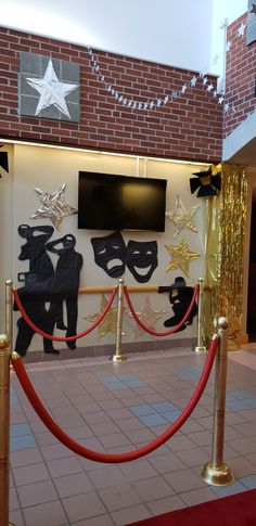 a red carpeted area with gold barriers and black masks on the wall behind it