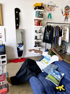 a man laying on top of a blue couch in a room filled with books and toys