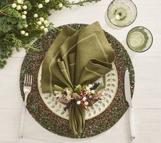 a place setting with green napkins, silverware and greenery on the table