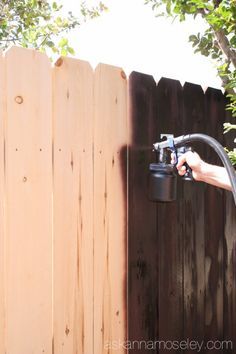 a man is spraying water from a hose attached to a wooden fence in the back yard