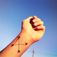 a hand holding up an arrow tattoo on it's left arm with the sky in the background