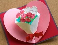 a heart shaped card with flowers in it on top of a red and pink envelope