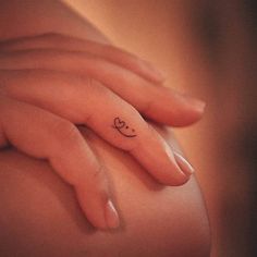 a woman's hand with a small heart tattoo on her left side ring finger