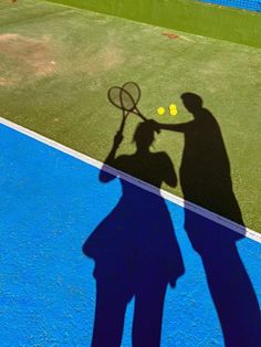 shadow of two people holding tennis racquets on a blue and green court