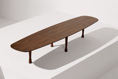 a wooden surfboard sitting on top of a white table next to a shadow cast wall