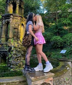 two young women are kissing each other in front of an old stone structure and water fountain