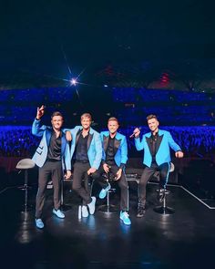 three men in blue jackets and black pants posing for a photo on stage at a concert