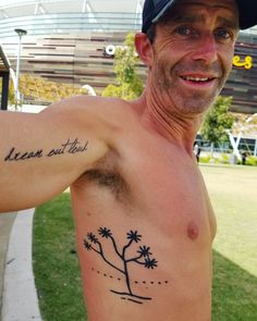 a man with a small tattoo on his arm and chest, standing in front of a stadium