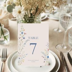 a table setting with flowers in a vase and place cards on the plate next to it