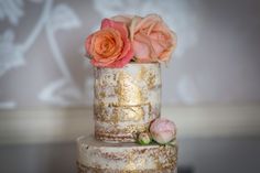 a three tiered wedding cake with pink roses on the top and gold leaf decoration