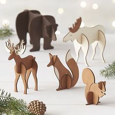 several wooden animals standing next to each other on a white surface with pine cones and lights in the background