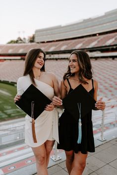 two women in graduation caps and gowns standing next to each other at a stadium