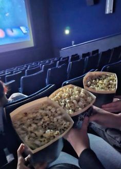 two people sitting in front of a movie theater holding up bowls of popcorn and watching movies