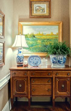 a painting hangs on the wall above a wooden table with blue and white vases