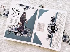 an open book with black and white flowers on the pages is sitting on a lace tablecloth