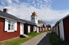 small red buildings with white windows and a church steeple in the background on a sunny day