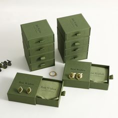 three green boxes with gold rings in them and some other jewelry items next to it