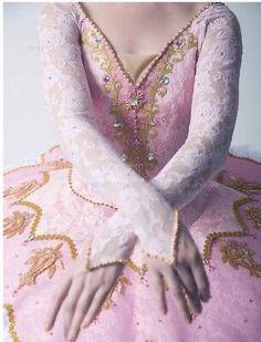 a woman in a pink dress with gold and white lace on her arms, sitting down