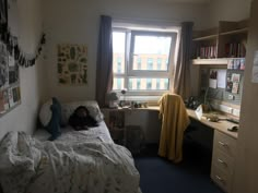 a small bedroom with a bed, desk and bookshelf next to a window