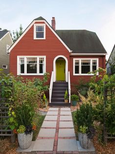 a red house with white trim and yellow door is surrounded by greenery, shrubs and trees