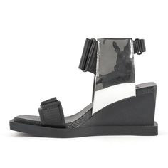 The Ko Mid is an updated sandal featuring UN's signature leather upper, nylon straps, a velcro closure, and a block wedge with a textured finish. The square-shaped EPR outsole and footbed offer a comfortable fit. Color: Black - Silver Mirror Standard Fit Heel Height: 80mm/3.2in Recycled leather upper with nylon webbing Leather lining PU footbed PU wedge heel Rubber outsole About the Brand: As the brain-child of architecturally-trained designer Rem D. Koolhaas (nephew and namesake of architect Re Modern Ankle Strap Sport Sandals In Synthetic, Modern Synthetic Sport Sandals With Ankle Strap, Modern Synthetic Ankle Strap Sport Sandals, Modern Sport Sandals With Buckle Closure, Modern Black Sport Sandals With Ankle Strap, Modern Black Ankle Strap Sport Sandals, Modern Leather Sandals With Translucent Outsole, Modern Open Toe Sport Sandals In Synthetic, Modern Open Toe Synthetic Sport Sandals