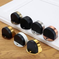 four black and gold knobs on a white door with wood flooring in the background