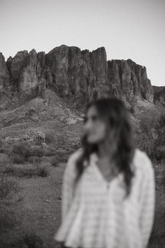 a woman standing in front of a mountain with her hair blowing in the wind and wearing a striped shirt