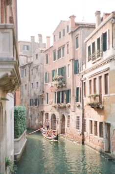 a small boat traveling down a river next to tall buildings with green shuttered windows