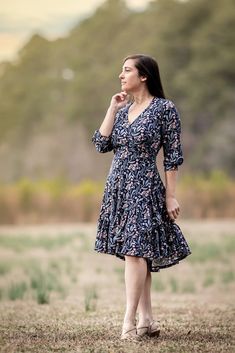 a woman standing in a field with her hand on her chin and looking up at the sky