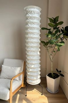 a tall white vase sitting next to a chair and a potted plant on top of a hard wood floor