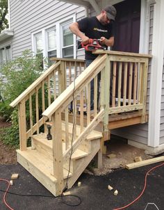 a man is working on a wooden stair rail outside his house with a power drill