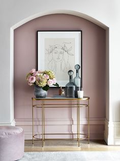 a table with flowers and vases on it in front of a pink painted wall