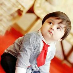 a young boy wearing a red tie and striped shirt sitting on the floor looking up