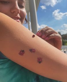 a ladybug tattoo on the arm of a girl with three small bugs on it