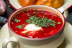 a bowl of soup with sour cream and herbs in it on a plate next to bread