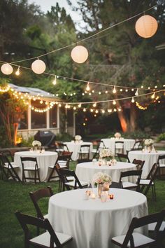 an outdoor dining area with white tablecloths and lights strung from the ceiling above